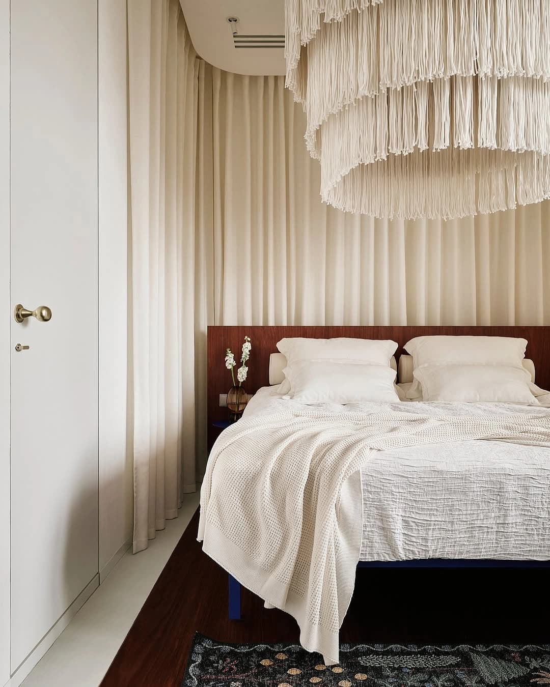 Quarto com cabeceira de madeira, cortinas e pendente de tecido.